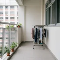 A balcony with potted plants along the railing and a clothes rack