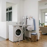 A washing machine, an ironing board and pressed shirts on a rail
